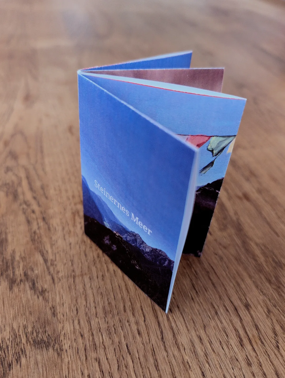 A folded Steinernes Meer photo zine standing on a wooden table.